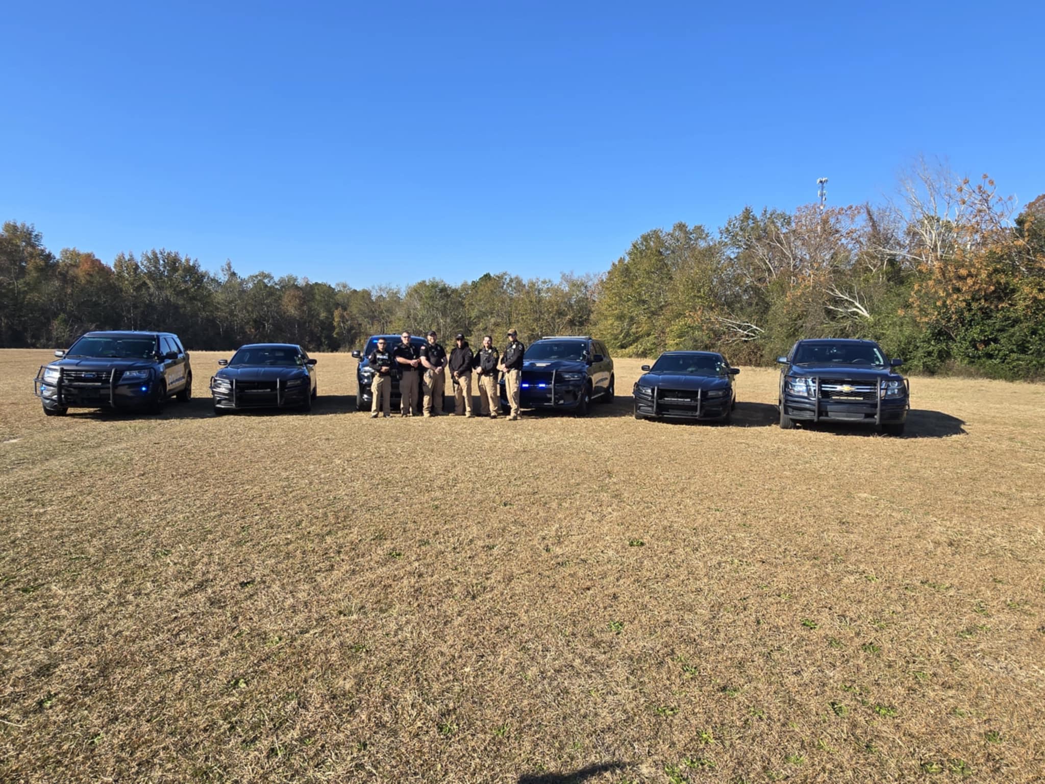 Photo of Police Dept employees standing in front of vehicles in a field